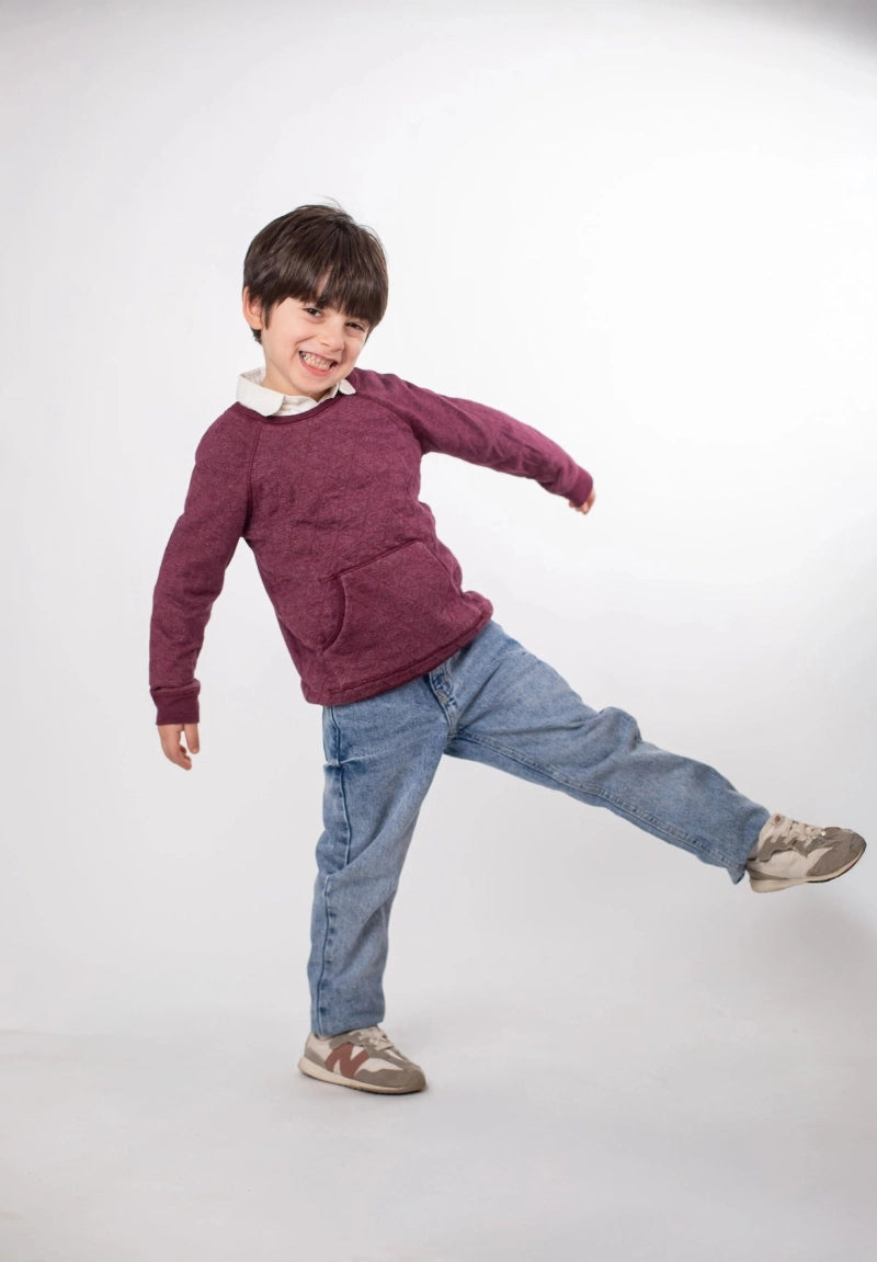 Child wearing a maroon sweater and blue jeans on a white background