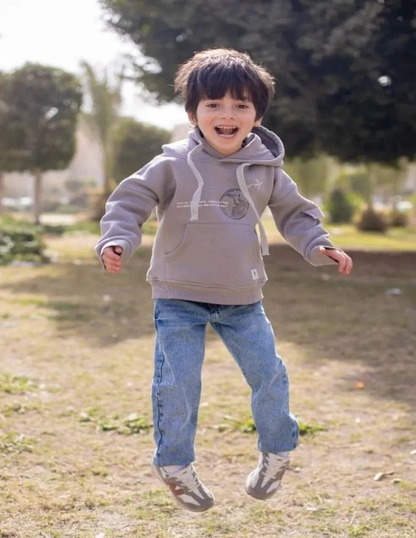 Child wearing a gray hoodie and blue jeans running outdoors on a grassy area.