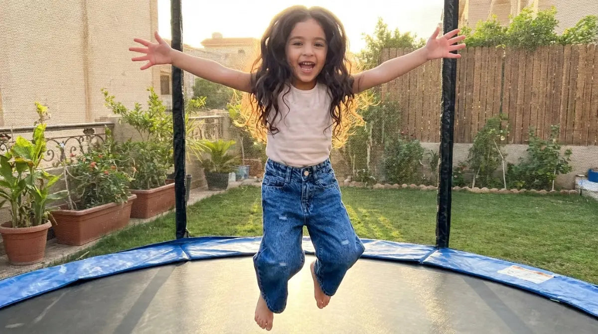 Child jumping on a trampoline in a backyard with plants and a fence in the background
