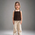 Young girl wearing a brown top and beige pants against a gray background