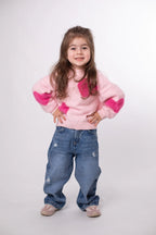 Child wearing a pink sweater with heart patterns and blue jeans on a white background