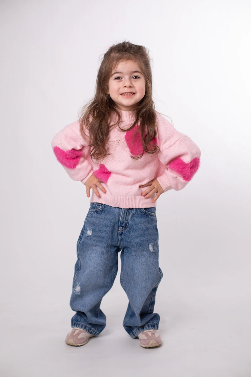 Child wearing a pink sweater with heart patterns and blue jeans on a white background