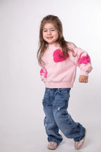 Child wearing a pink sweater with heart designs and blue jeans on a white background