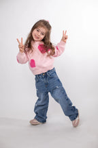 Child wearing a pink sweater with heart designs and blue jeans on a white background
